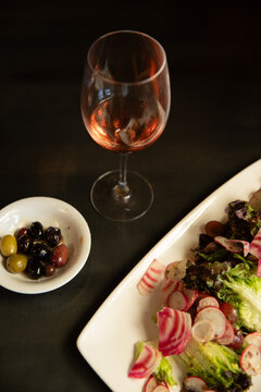 overhead shot of lettuce and radish salad with side of mixed olives and wine