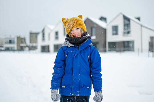 Happy young child playing with fresh snow in the backyard on a winter day. Smiling kid holding snow in gloved hands and enjoying outdoor seasonal activity.
