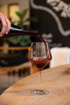 sommelier pouring red wine into a glass with background of winery tasting room blurred out