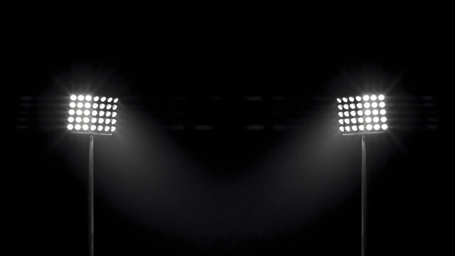 Two tall stadium floodlight towers glowing brightly against a dark night sky, illuminating the surrounding area with intense white light beams