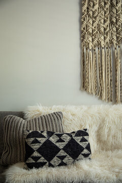 boho living room vignette with sheepskin throw, hanging macrame, and knitted throw pillows in neutral color palette