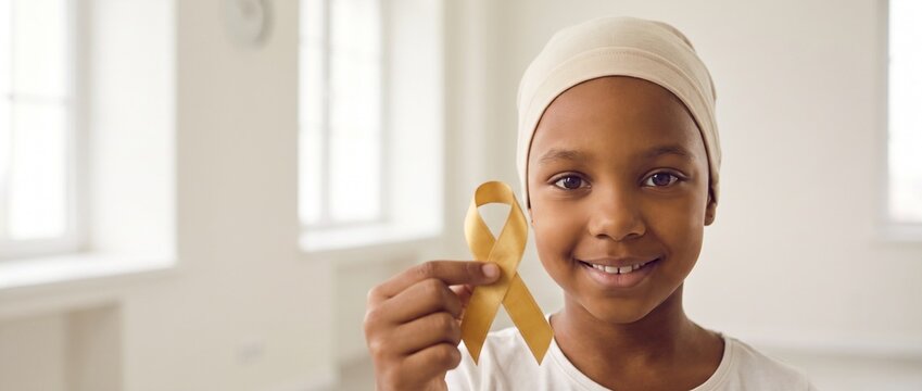 Crian&ccedil;a negra com touca sorrindo e segurando la&ccedil;o dourado. Banner de conscientiza&ccedil;&atilde;o do c&acirc;ncer infantil e leucemia no Setembro Dourado. Muito espa&ccedil;o para texto