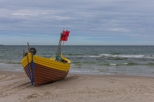 Front view of traditional wooden fishing boat with red flags on Baltic beach