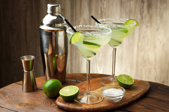 Delicious margarita cocktail in glasses, fresh fruits, salt, shaker and jigger on wooden table