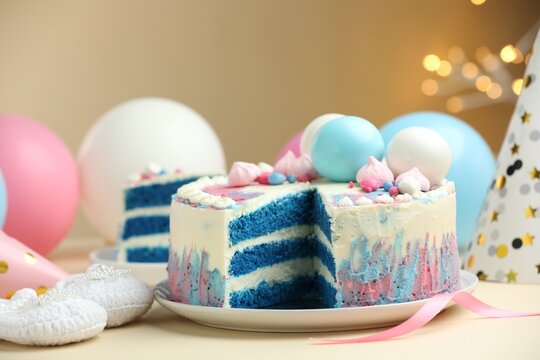 Decorated gender reveal cake with blue layers and balloons on beige table against blurred lights, closeup. Bokeh effect
