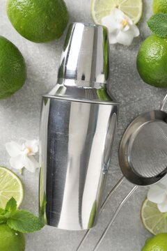 Shaker, limes, sieve, mint and orchid flowers on grey table, flat lay