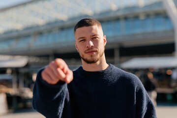 Fototapeta premium Young man pointing at camera portrait in urban street for recruitment call to action banner and marketing background