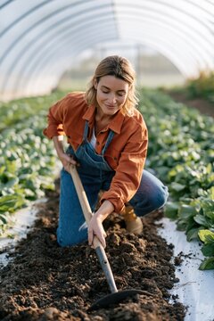 Female farmer digging soil in greenhouse organic vegetable bed for gardening background and farmwork banner