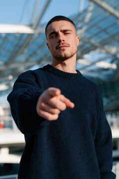 Confident young man pointing at camera outside a modern transport hub for recruitment poster and social media banner