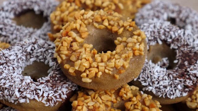 Donut assortment fills frame with coconut and nut toppings. Sweet pastries rest tightly stacked in closeup, creating rich bakery texture and inviting dessert display for festive catering or sale.