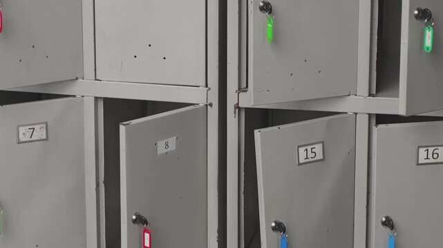 The metal lockers in a school, gym, or factory changing room are shutting one after another. Each locker has a key with a vibrant tag hanging from the lock