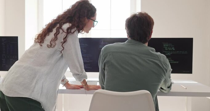 Engineers review programming code on computer monitors. Developers collaborate in a bright office, discussing software details and teamwork. Ideal for technology collaboration campaigns.