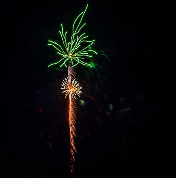 Fireworks light up the night sky with bright colors including green and orange. The display happens during a celebration in the city, creating excitement among the crowd below.