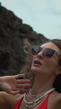 Glamorous female traveler wearing chic eyewear relaxing near rugged geological formations. Medium close-up static shot.