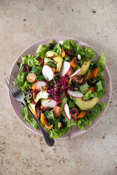 Over the top view of a pixbae fruit salad with lettuce, avocado, olives, pistachio, radicches.