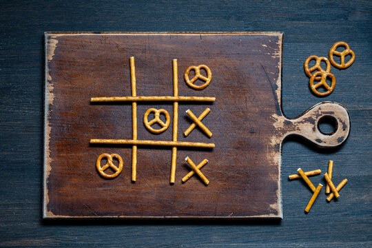 Tic tac toe game made of pretzel sticks and twists top view, closeup. Creative tic-tac-toe game laid out with salty pretzel sticks and twists on rustic wooden cutting board, flat lay photography
