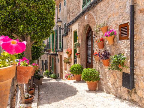 Narrow alleyway with potted flower pots hanging on stone house walls in the historic village of Valldemossa Mallorca Spain