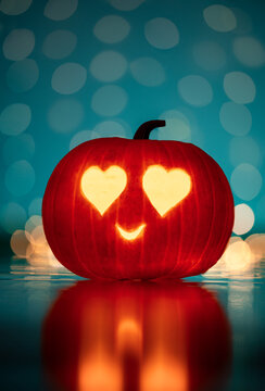 Single glowing Halloween jack-o'-lantern pumpkin with heart-shaped eyes and smiling face, beautiful autumn decoration with teal background, warm bokeh, and reflection