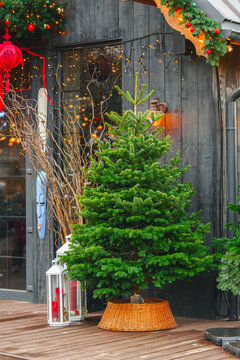 Christmas tree decorated with delicate lights outside of modern storefront, surrounded by warm golden bokeh and festive decorations, creating a cozy Christmas mood and holiday atmosphere.