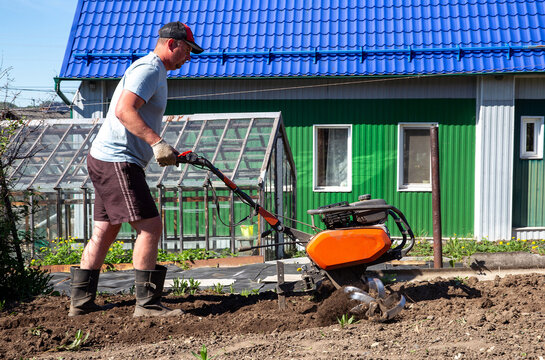Hardworking gardener skillfully operating a powerful motorized cultivator on plantation, preparing rich soil for planting potatoes and various crops