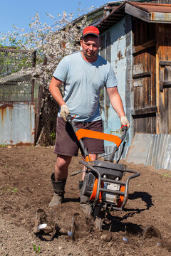 Hardworking gardener skillfully operating a powerful motorized cultivator on plantation, preparing rich soil for planting potatoes and various crops