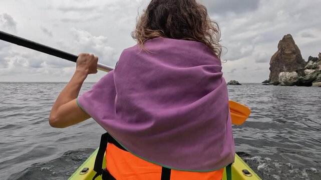 Navigating coastal waters by kayak toward towering sea stacks. Rear-angle tracking shot captures rhythmic oar movement.