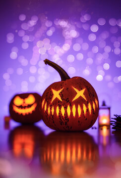 Glowing Halloween jack-o'-lantern pumpkin with star-shaped eyes and sharp teeth, beautiful spooky autumn scene with purple bokeh, reflection, and second carved pumpkin