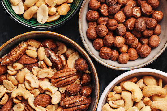 Mixed nuts arranged in ceramic bowls background. Cashews hazelnuts peanuts almonds and pecans provide crunchy snacks. Assorted natural foods contain plant protein. Nut selection for everyday eating.