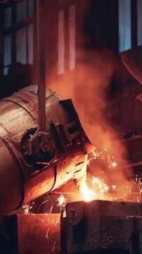 Liquid metal in heavy industry manufacturing foundry, intense heat, sparks and smoke during smelting and metalworking inside factory. Vertical video
