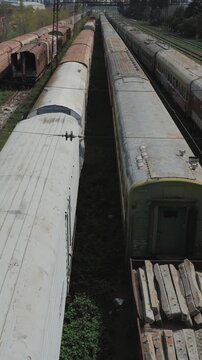 Abandoned railway yard with old passenger trains and rusty railcars, elevated view of obsolete transport infrastructure, decay and industrial decline, Vertical Video.