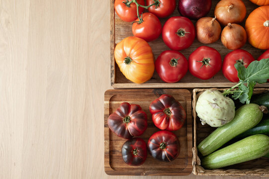 Tomatoes, onions, squash in boxes on wooden table background with natural light, top view, copy space. Fall vegetable food market produce