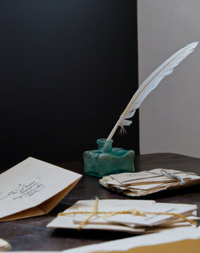 White Feather Quill in Inkwell on Vintage Desk with Old Letters
