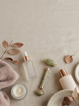 Flat lay of unlabelled skincare bottles a jade roller and dry autumn leaves on linen