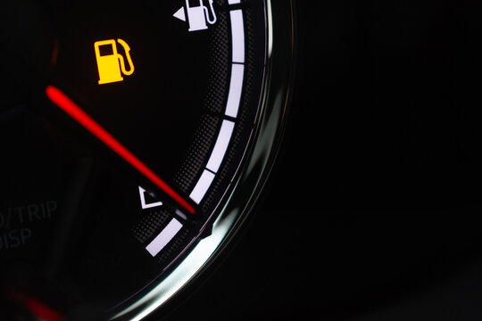 Close-up of low fuel warning light icon illuminated on black car fuel gauge indicator