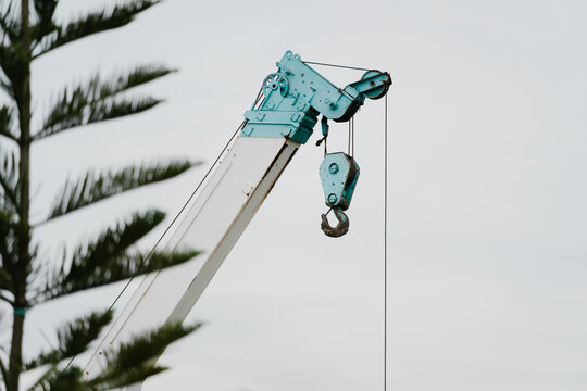 Heavy lifting crane boom hook industrial construction machine machinery blue equipment outdoors engineering site against pine tree foliage