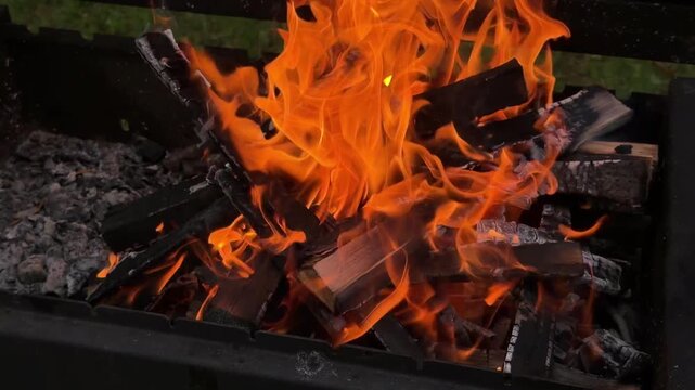 Horizontal 4K video of a bright campfire burning in a metal brazier outdoors with vibrant orange and red flames over wood logs.
