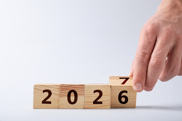 New Year. Man flipping wooden cube with numbers - changing 2026 to 2027 against white background,...