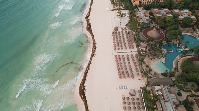 Aerial view of a resort coastline with pale sand and turquoise waves rolling ashore