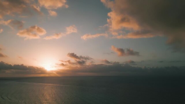 Sun setting behind soft clouds over a tranquil ocean horizon