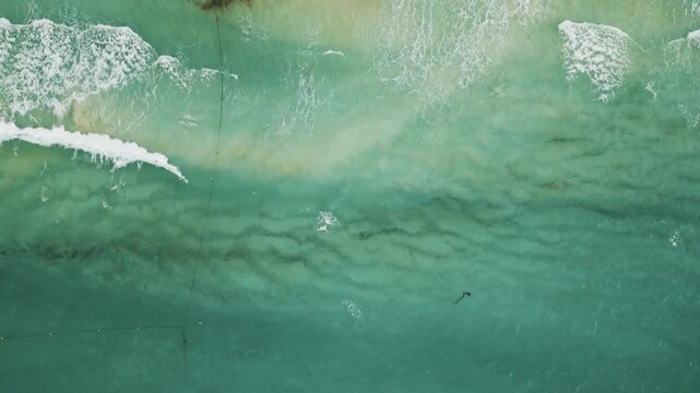 Aerial view of turquoise waves rolling over scattered seaweed streaks