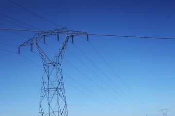 Vue en perspective d'un pylône électrique en ossature métallique, portant des lignes à haute tension. Structure dédiée au transport de l'énergie par voie aérienne. Ciel bleu en arrière plan. © Xavier