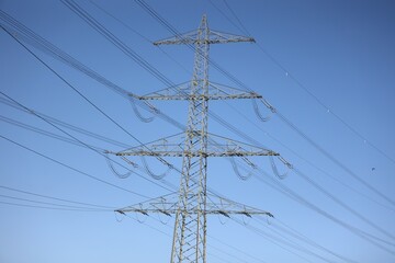 Vue en perspective d'un pylône électrique en ossature métallique, portant des lignes à haute tension. Structure dédiée au transport de l'énergie par voie aérienne. Ciel bleu en arrière plan. © Xavier