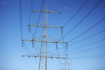 Vue en perspective d'un pylône électrique en ossature métallique, portant des lignes à haute tension. Structure dédiée au transport de l'énergie par voie aérienne. Ciel bleu en arrière plan. © Xavier