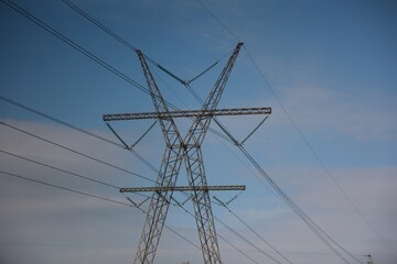 Vue en perspective d'un pylône électrique en ossature métallique, portant des lignes à haute tension. Structure dédiée au transport de l'énergie par voie aérienne. Ciel bleu en arrière plan. © Xavier