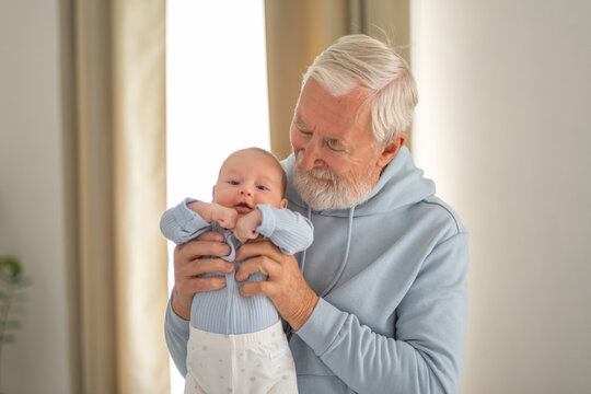 Grandfather looks down at baby held in his strong arms, grandfather present from very beginning, warmth passed between generations. Wide shot. Concept of grandfather holding newborn grandson