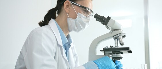 Dedicated female scientist working with a microscope in a modern laboratory, performing cellular...