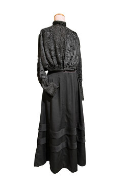 Antique, two-piece walking suit from the turn of the 20th century (Edwardian or late Victorian era), made of black wool and silk, featuring decorative lace and a high collar.