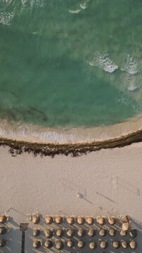 Static aerial view of turquoise waves meeting a sunlit resort beach