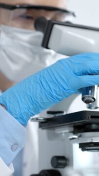 Scientist in blue protective gloves rotating the objective lens of an optical microscope. Conducting essential biological research. Medical analysis
