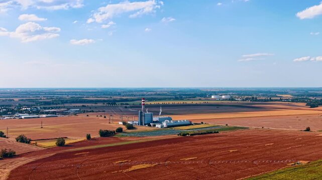 Bare brown agricultural fields with a plant facility in the middle. Drone footage approaching the industrial area in the vast countryside.